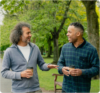 Two men walking and talking in a park. The path and trees can be seen behind them.