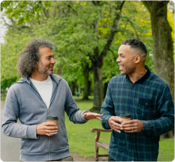 Two men walking and talking in a park. The path and trees can be seen behind them.)