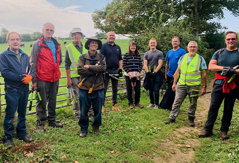 Volunteers in a group standing for a picture next to a fence. Rolling fields are visible in the background.