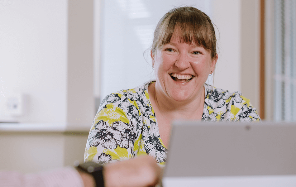 A woman using a laptop smiling, looking just away from the camera.