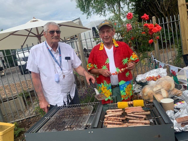 Two people smiling, stood in front of a BBQ.