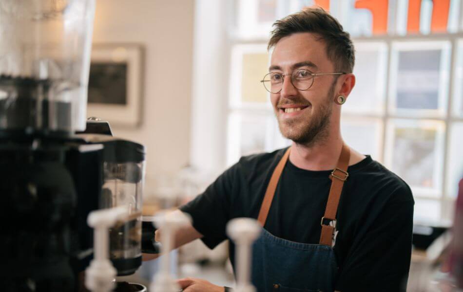 Martin looking down as he's preparing a coffee. He's in his apron, smiling.