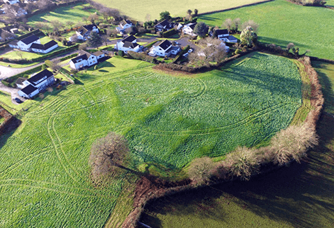 A village hamlet seen from the air. Houses clustered next to lush green fields can be see in the areal shot.