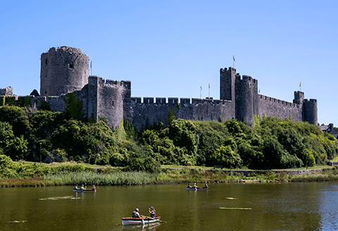 Pembroke Castle seen from a distance. Lush green foliage can been seen creeping up the walls of the fortress.