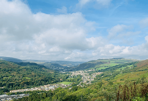 A valley seen from the air. The sky is bright and the rolling hills are a lush green.